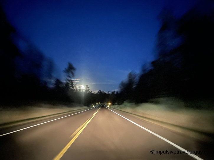 Night driving on two-lane highway with yellow center line, headlights of oncoming vehicle visible, motion blur from trees on sides