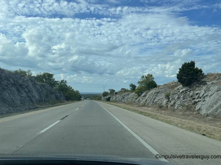 Highway cutting through exposed limestone rock walls on both sides under partly cloudy sky