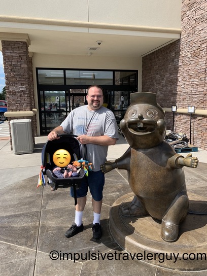 Man with child in stroller posing beside large bronze Buc-ee's beaver mascot statue at store entrance