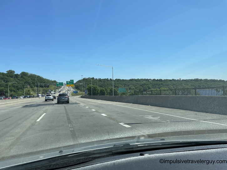 Highway bridge crossing over a lake with forested shores, taken from inside a vehicle traveling on a multi-lane interstate highway on a clear day