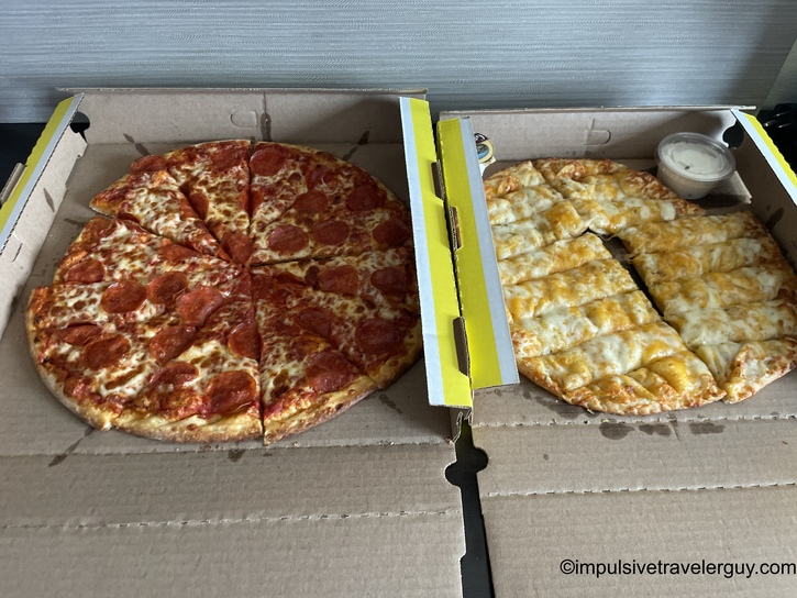 Two pizzas in delivery boxes - one pepperoni pizza and one white pizza with ranch dressing cup, corrugated cardboard visible