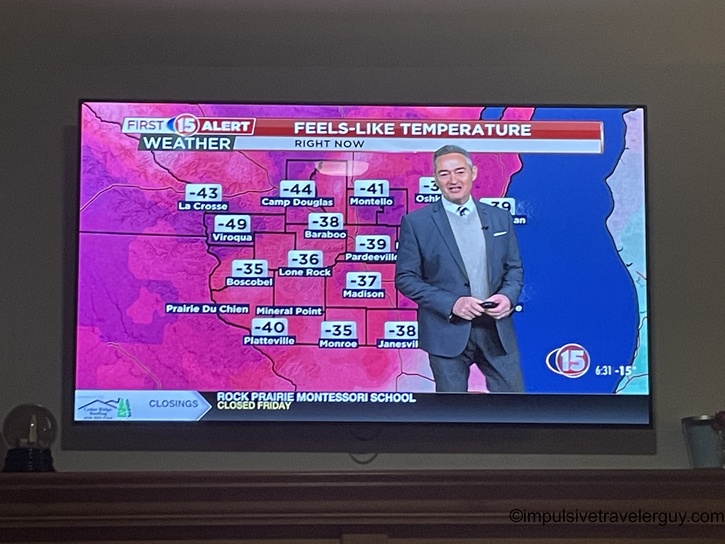 A television displaying a Channel 15 First Alert Weather broadcast showing "feels-like temperature" readings across southern Wisconsin, with values ranging from -35°F to -49°F in various cities including Madison at -37°F.