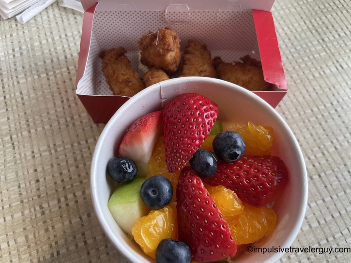 A meal from Chick-fil-A featuring a red box of chicken nuggets and a white cup of fresh fruit containing strawberries, blueberries, mandarin orange segments, and honeydew melon pieces.