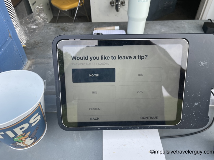 Square tablet point-of-sale screen prompting for a tip on a $26.32 total with No Tip, 10%, 15%, 20%, and Custom options, next to a duck-themed TIPS bucket on a concession counter