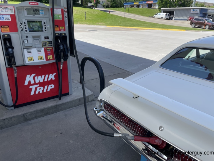 The Cougar's rear end pulled up to a Kwik Trip pump for fuel, nozzle inserted in the filler behind the rear license plate, pump display showing $6.94 and 1.362 gallons with 87, 88, and 91 octane options visible.