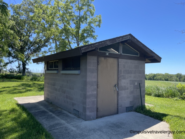 A shuttered cinder-block restroom building at the rest area, with a dark brown steel door, clerestory windows, and a low-pitched shingled roof showing its age.