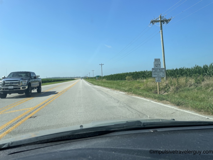 Driving south on Illinois Route 127 through flat cornfield country with a Ford pickup passing in the opposite lane and a bridge weight limit sign ahead.