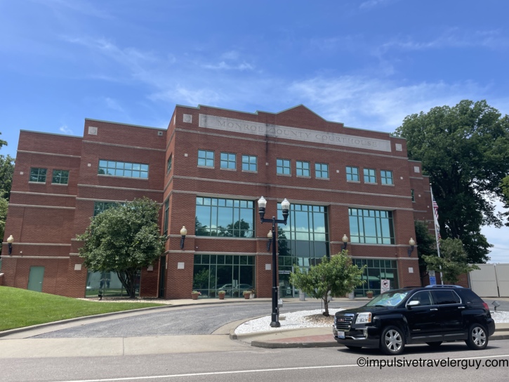 Monroe County Courthouse, a modern three-story red brick building with large glass windows, decorative street lamps, and carved stone nameplate across the top.