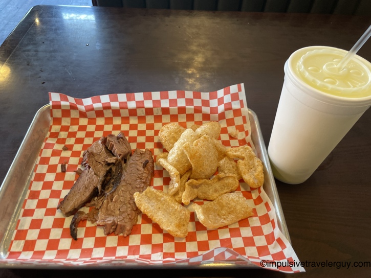 Smoked brisket and pork rinds served on red-and-white checkered paper in a metal tray with a large lemonade at Shorty's Smokehouse.