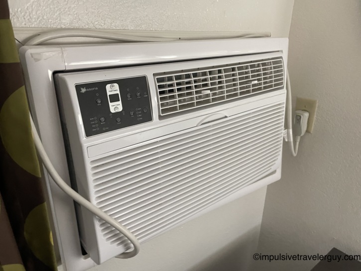 Wall-mounted Seasons brand through-the-wall air conditioning unit with digital control panel in the motel room, powered off.