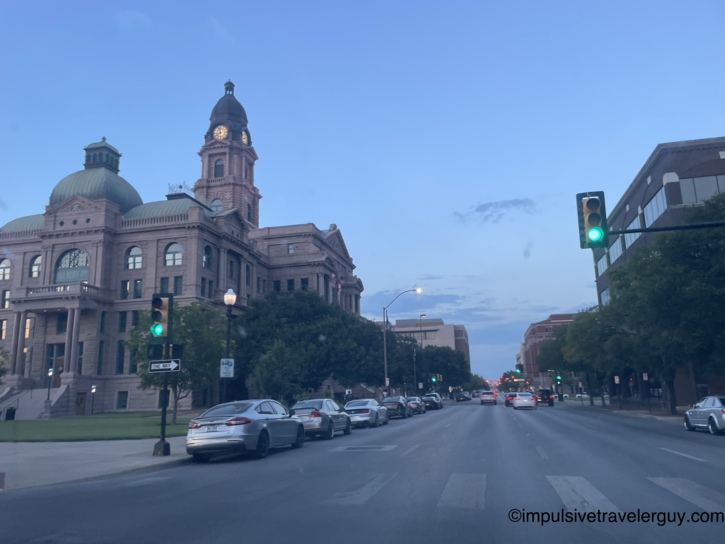 View from a vehicle driving down a Fort Worth street, passing the actual historic courthouse building featured on the map.