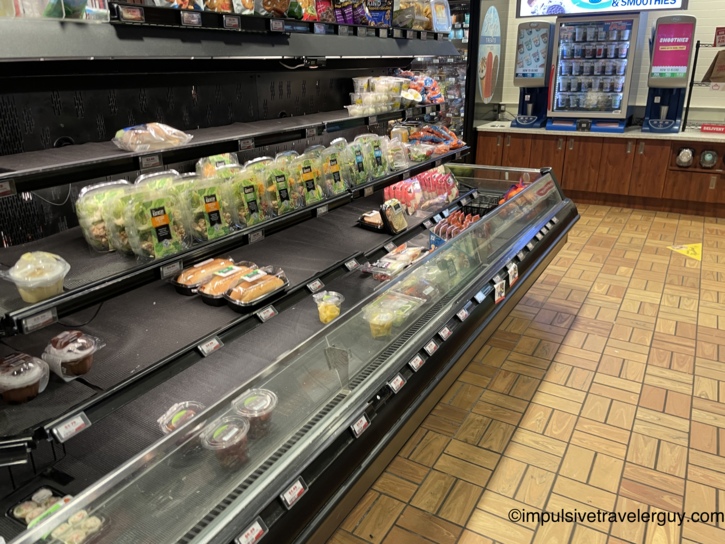 An understocked refrigerated food display case in the convenience store containing a few pre-packaged salads and sandwiches.