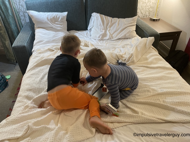 Two young children in pajamas kneeling on a pulled-out sofa bed while looking at a tablet together.