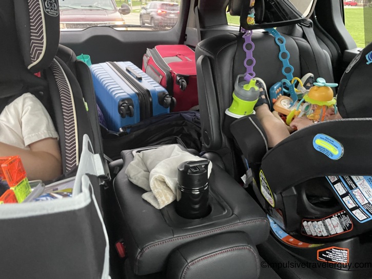 Interior view of a family vehicle's back seats and cargo area, showing two child car seats and luggage packed for the road trip to Texas.