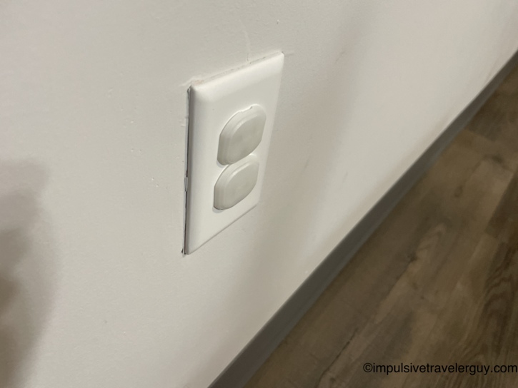 Close-up of a white electrical wall outlet fitted with clear plastic child safety plug covers for baby-proofing.