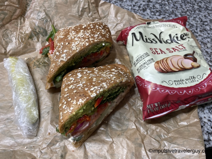 A halved veggie sandwich from McAllister's Deli served alongside a bag of Miss Vickie's Sea Salt chips and a pickle spear.