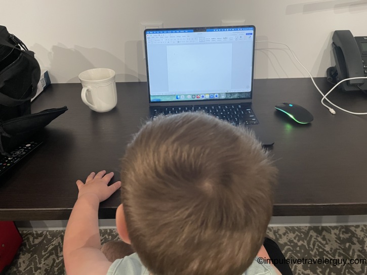 Over-the-shoulder view of a small child sitting at a desk looking at a laptop displaying a blank Word document.
