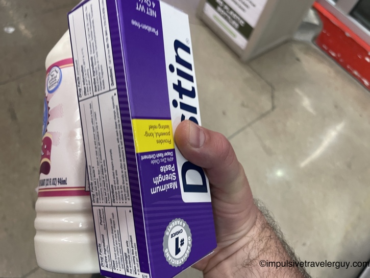 A hand holding a box of Desitin diaper cream and a bottle of milk in an H-E-B store aisle.