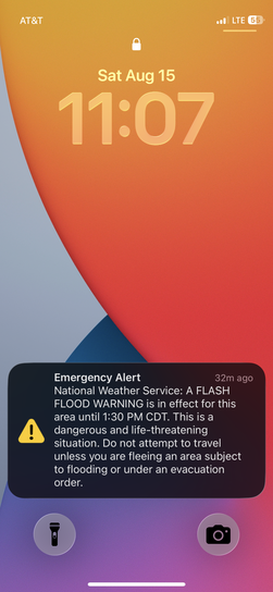 Smartphone lock screen showing an emergency alert from the National Weather Service for a Flash Flood Warning during the drive.